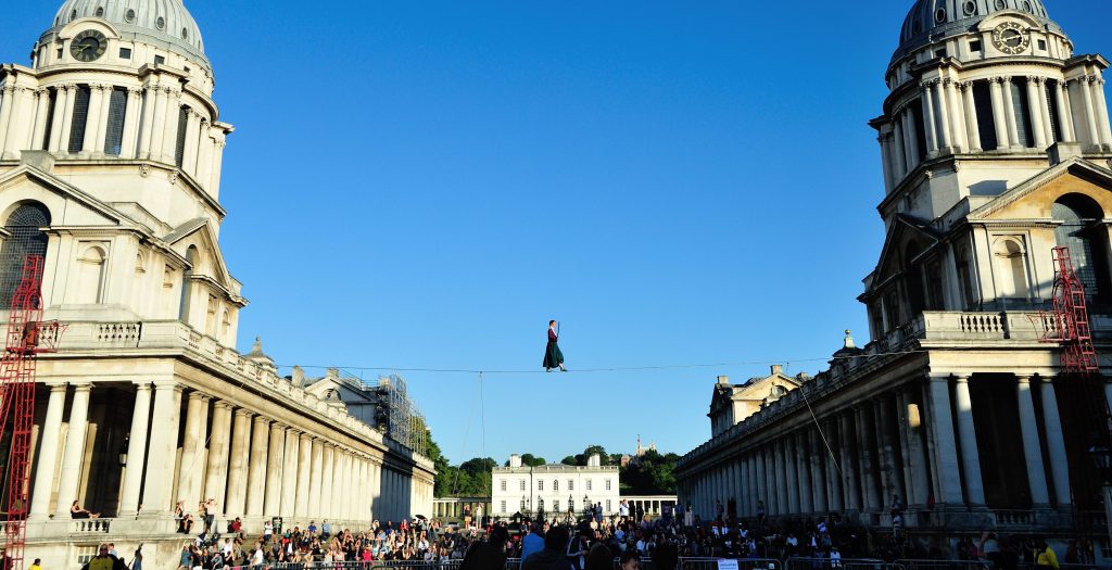 Photograph of a funambulist walking the tightrope suspended between the twin domes of the Old Royal Naval College during Greenwich+Docklands International Festival 2018