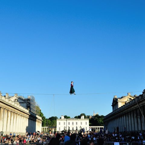 Photograph of a funambulist walking the tightrope suspended between the twin domes of the Old Royal Naval College during Greenwich+Docklands International Festival 2018