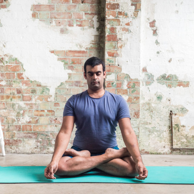 Yoga practitioner Rishin Paonaskar meditating in a well-lit room with brick walls.
