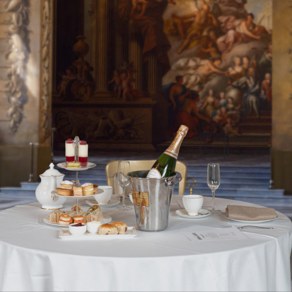 A table in the Painted Hall with a white table cloth, set with afternoon tea and champage. 